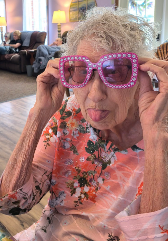 A resident wearing enormous pink rhinestone sunglasses and sticking out her tongue playfully in the Lavender Fields living room