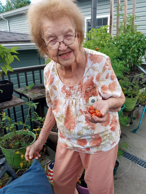 Ruth standing in the garden holding a handful of cherry tomatoes she just picked, grinning
