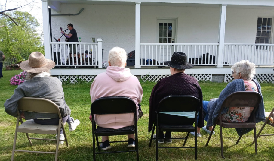 Residents seated on the lawn watching a live concert on the porch at the Beverly Heritage Center